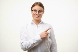 Glad young lovely blonde woman in glasses keeping forefinger raised while pointing cheerfully aside and smiling widely, isolated over white background photo