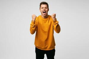 Young happy man with really impressive achievements, giving a fists up gesture of victory, rewarded, won a good prize, successful deal, positive news, screaming with happiness, over white background photo