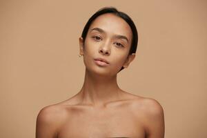 Portrait of an attractive charming caucasian girl, looking camera like in the mirror, after a facial treatment, head slightly turned and tilted,with fresh skin after the procedure, beige background photo