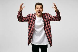 Emotional young guy is happy, cheerful, arms raised up stretched forward as if glad to meet or is going to hug someone, mouth opened, wearing a checkered shirt, over white background photo