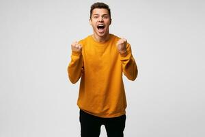 Man celebrates winning of his favorite football team, giving a fists up gesture of victory, incredibly pleased with the success, screaming with happiness, over white background photo