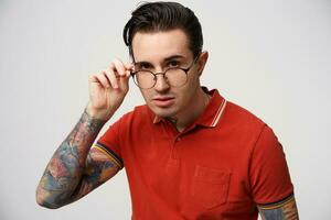 A man is looking strictly at the camera with lowered glasses, holds rim, isolated over white background. Angry displeased with what is happening photo