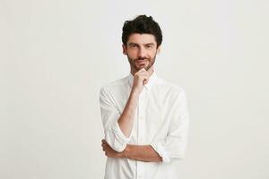 Portrait of thoughtful attractive young businessman with bristle wears shirt looks pensive and confident isolated over white background Keeps hands folded photo