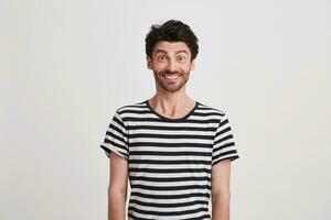 Portrait of happy attractive young man with bristle wears striped t shirt feels excited and smiling isolated over white background Looks directly in camera photo