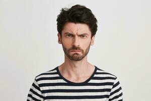 Portrait of angry displeased young man with bristle wears striped t shirt looks serious and irritated isolated over white background photo