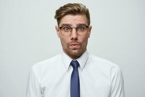 Amazed man dressed white shirt and tie, stares through glasses, being surprised find out about his success. Male doesnt believe his own luck, isolated over white background.People emotions concept photo