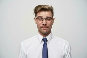 simpático joven hombre muestra atención, mira calma, guiños, alegre, lindo, trabajos como un consultor o Tienda gerente. vistiendo un blanco camisa y azul atar, con anteojos, en un blanco antecedentes. foto