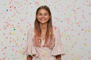 Closeup of cheerful attractive young woman with long dyed pastel pink hair wears polka dot pink dress having fun and celebrating birthday isolated over white background with confetti photo