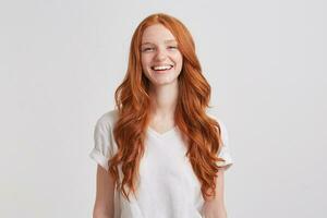 Portrait of cheerful cute redhead young woman with long wavy hair and freckles wears stylish t shirt looks relaxed and laughing isolated over white background Feels happy photo