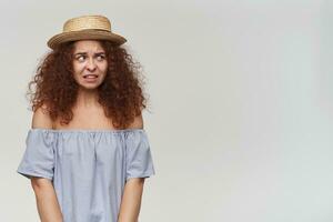 Portrait of afraid, adult redhead girl with curly hair. Wearing striped off-shoulders blouse and hat. Feels sorry for you. Watching to the right at copy space, isolated over white background photo