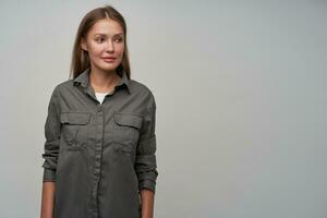 Teenage girl, cute looking woman with brown long hair. Looking at something with concentration. Wearing grey shirt and watching to the right at copy space, isolated over grey background photo