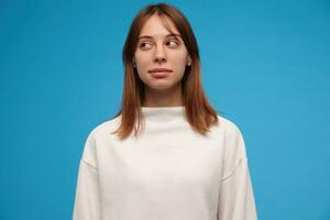 Nice looking woman, beautiful girl with brunette hair. Wearing white sweater. People concept. Casual looking. Suspiciously watching to the left at copy space, isolated over blue background photo