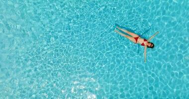 topo baixa Visão do uma mulher dentro vermelho roupa de banho deitado em dela costas dentro a piscina. video