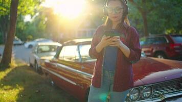 Woman is standing outdoors near the red vintage car and using smartphone video