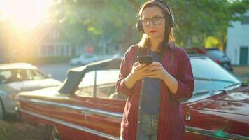 Woman is standing outdoors near the red vintage car and using smartphone video