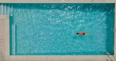 parte superior abajo ver de un hombre en rojo pantalones cortos nada en el piscina. lento movimiento video