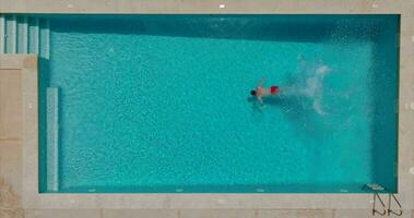 Aerial view as a man dives into the pool and swims. Slow motion video