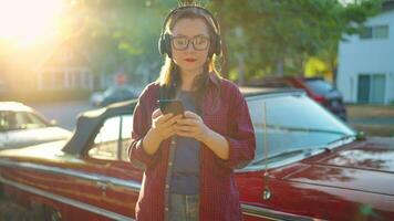 Woman is standing outdoors near the red vintage car and using smartphone video