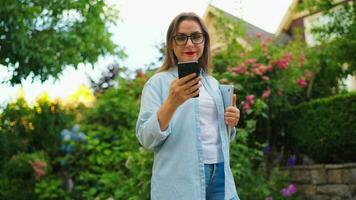 mujer con ordenador portátil y teléfono inteligente en pie en el floreciente jardín video