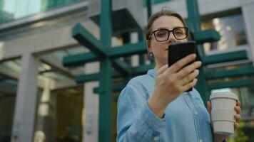 Caucasian woman in glasses stands on the street and using smartphone video