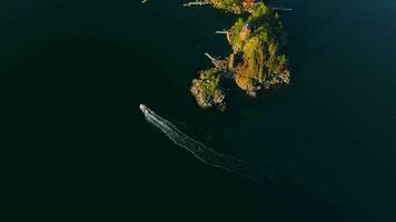 Top down view of motor boat sails around the coast of the island. Camera rotates video