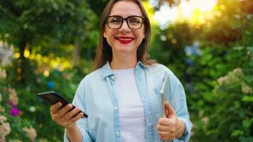 Woman with laptop and smartphone standing in the blooming garden video