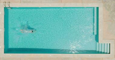 Aerial view as a man dives into the pool and swims. Slow motion video