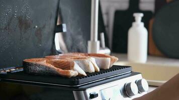 Woman cooking salmon steaks on modern electric grill in the kitchen video