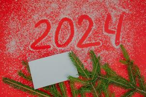 From the numbers 2024 on a red background with spruce branches, the concept of the New Year holiday photo