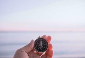 Close up hand holding compass with beach background photo