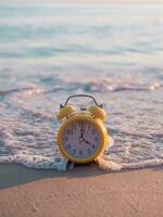 amarillo alarma reloj en el playa en el puesta de sol tiempo. el concepto acerca de hora a verano, viajar, vacaciones y relajación foto