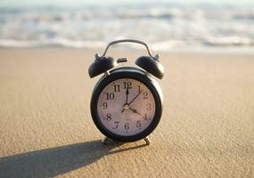 negro alarma reloj en el playa en el puesta de sol tiempo. el concepto acerca de hora a verano, viajar, vacaciones y relajación foto