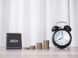 2024 escritorio calendario, negro alarma y apilar de monedas el concepto de ahorro dinero y gestionar hora para financiero, inversión y negocio creciente en nuevo año 2024. foto