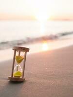 Hourglass on the beach in the sunset time. The concept about countdown to Summer, Travel, Vacation and Relaxation. photo