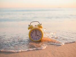 Yellow alarm clock on the beach in the sunset time. The concept about Time to summer, Travel, Vacation and Relaxation photo