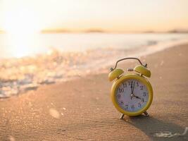 Yellow alarm clock on the beach in the sunset time. The concept about Time to summer, Travel, Vacation and Relaxation photo