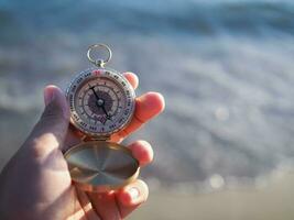 Close up hand holding compass with beach background photo