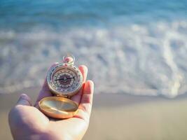 Close up hand holding compass with beach background photo