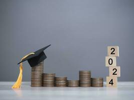 Wooden block with number 2024 and graduation hat on stack of coins. The concept of saving money for education, student loan, scholarship, tuition fees in Year 2024 photo