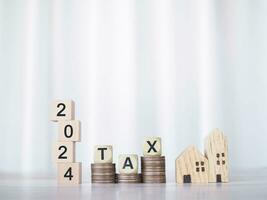 Miniature house, Wooden blocks with the word TAX and number 2024 on stack of coins. The concept of payment tax for house, Property investment, House mortgage, Real estate in New Year 2024. photo