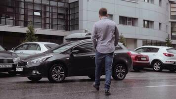 A young handsome businessman with a short haircut goes to his parked car in black and sits in it video