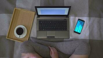 Overhead shot, creative girl in stockings working using a laptop sitting on the bed, eating a donut and drinking coffee video