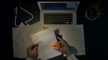 A man marks the words in documents while sitting at a table with a laptop. overhead shot video