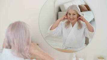 Skin Care, Senior Woman, Home Cosmetics, Elderly Age, Cosmetic Procedures. 70 year old woman in a bathrobe smooths her face with her hands in front of a mirror video