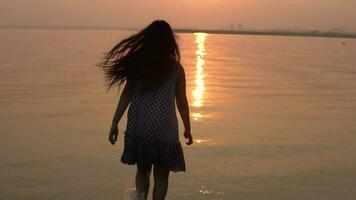 un' ragazza con lungo capelli corre in il acqua su un' tramonto sfondo. lento movimento. video