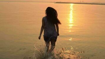 une fille avec longue cheveux court dans le l'eau sur une le coucher du soleil Contexte. lent mouvement. HD video