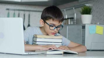 une enfant avec des lunettes Faire devoirs tandis que en train de lire une cahier de texte avec le sien tête repos sur une empiler de manuels. video