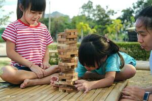 niños emocionados y mamá jugando al juego de bloques de madera de la torre jenga juntos en el parque. familia feliz con niños disfrutando juntos de las actividades de fin de semana. foto