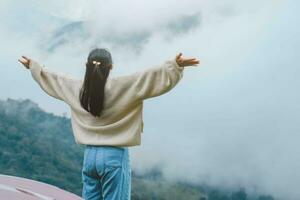 Rear view of a young woman standing on the top of a calm mountain and looking at the morning clouds. Woman wearing a sweater enjoying the beauty of nature looking at the mountain in winter. photo