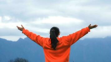 Rear view of a young woman standing on the top of a calm mountain and rising hands on mountain in morning. Woman wearing a sweater enjoying the beauty of nature looking at the mountain in winter. photo